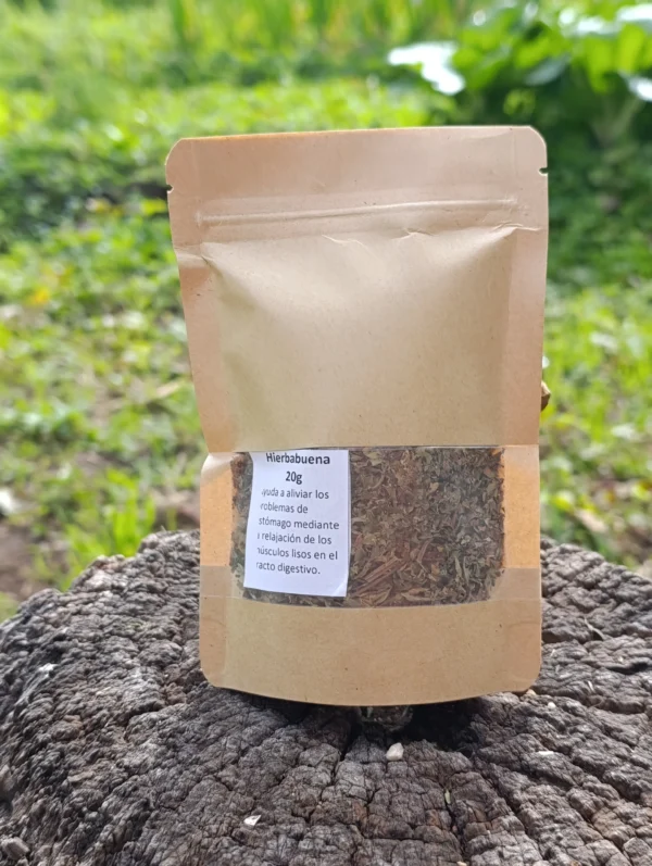 Bolsa ecológica de hierbabuena molida sobre tronco de madera en entorno natural.
