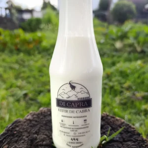Botella de kéfir de cabra artesanal sobre tronco en ambiente verde.