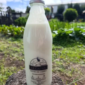 Botella de kéfir de cabra artesanal sobre tronco en ambiente verde.