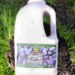 Botella de yogur artesanal de arándano de la marca Mi Finca sobre tronco natural.