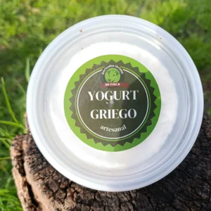 Envase redondo de yogurt griego artesanal Mi Finca sobre tronco natural al aire libre.