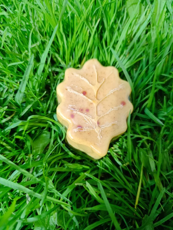 Jabón artesanal en forma de hoja sobre pasto verde, con cúrcuma natural y pétalos integrados, ideal para el cuidado de la piel.