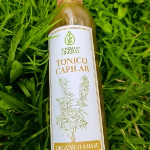 Botella de tónico capilar Rosemary Herbal con romero y jengibre sobre césped verde.