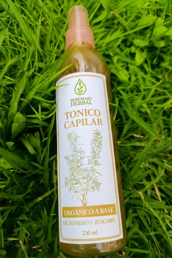 Botella de tónico capilar Rosemary Herbal con romero y jengibre sobre césped verde.