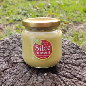 Frasco de hummus de garbanzo artesanal sobre tronco en ambiente natural.