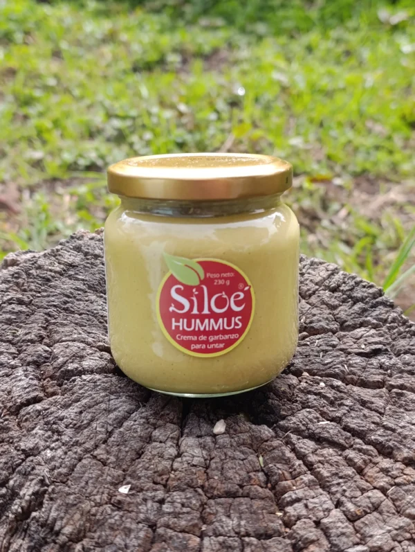 Frasco de hummus de garbanzo artesanal sobre tronco en ambiente natural.