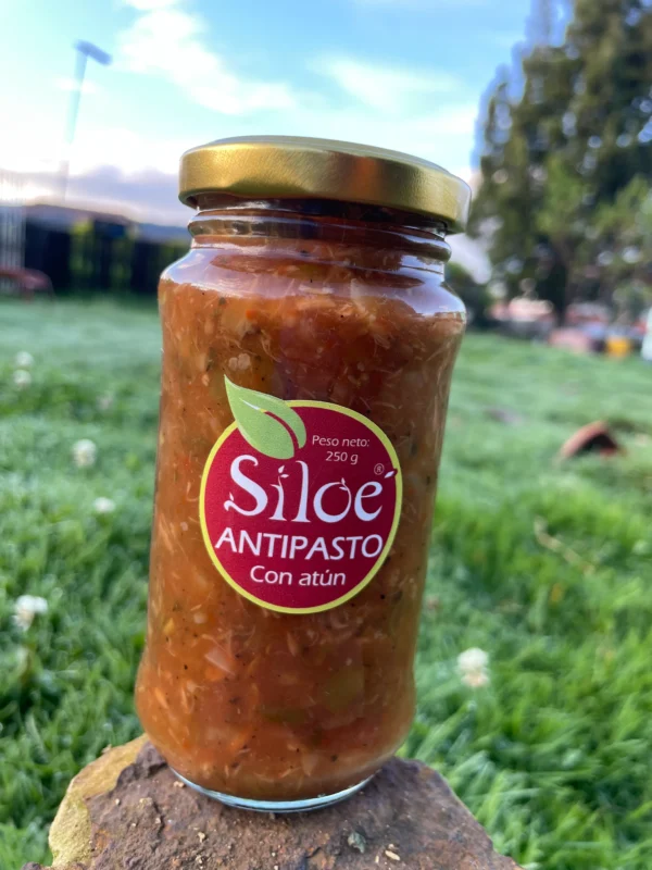 Antipasto casero con atún presentado en frasco de vidrio, sobre fondo natural.