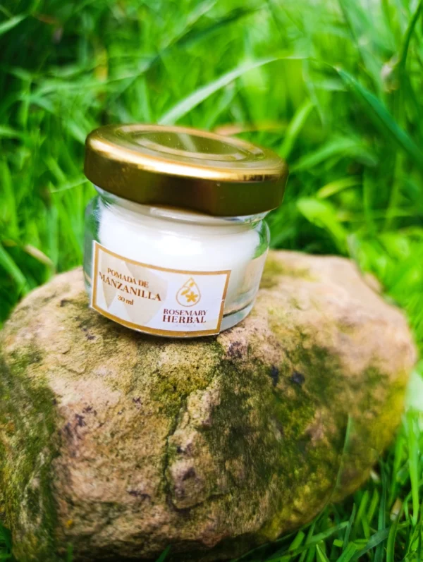 Frasco de pomada de manzanilla Rosemary Herbal de 30 ml sobre piedra, con fondo de pasto verde.